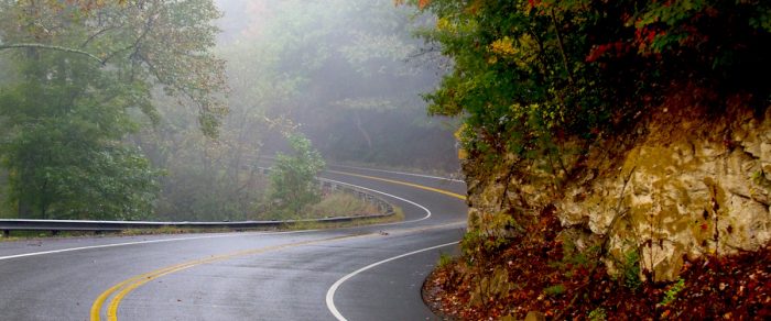 A curving country road winds past a pale cliff and forest in West Virginia