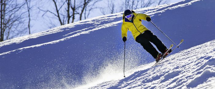 Skier in yellow coat skis over blue, snowy slopes at Winterplace, WV