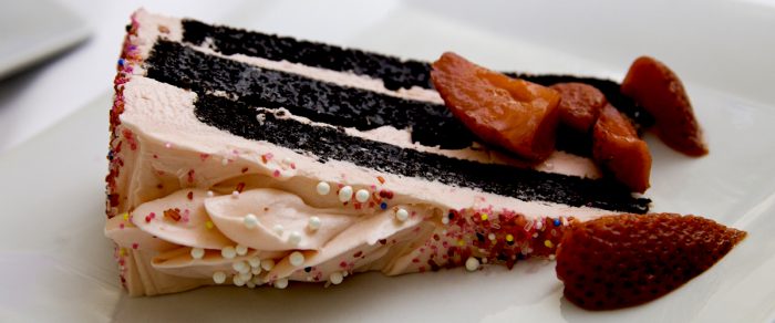 Devil's Food Cake slice with pink icing, sprinkles, and strawberries. The French Goat, WV