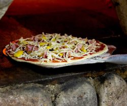 Pizza with cheese, ham, and pineapples going into oven, WV