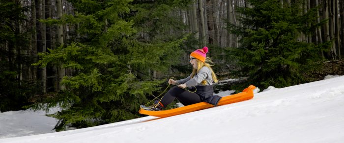 Young woman on orange sled going downhill at Blackwater Falls State Park, WV