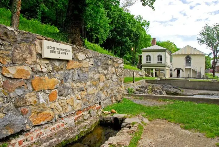 Stone wall with sign for George Washington Bath House and historic buildings nearby