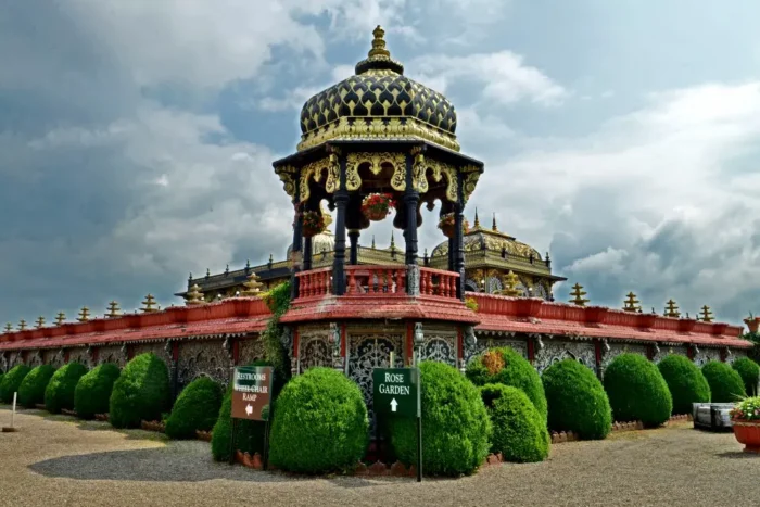 Ornate pavilion with gold dome and carved details surrounded by manicured garden shrubs