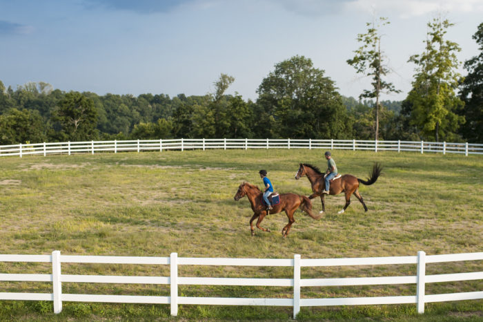 Two horseback riders riding through white fenced grassy area