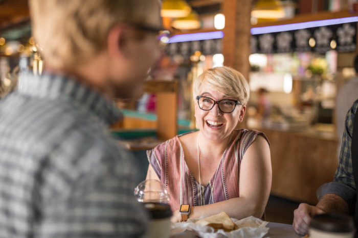 Blonde woman with glasses sitting in a restaurant smiling and laughing at a man