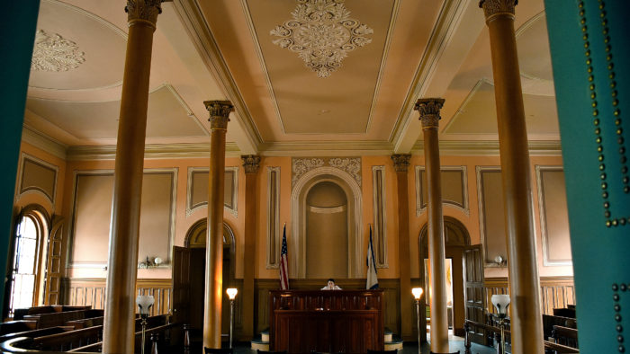 Inside the West Virginia Independence Hall with tall golden pillars and decorated ceilings, surrounded by rows of seats 