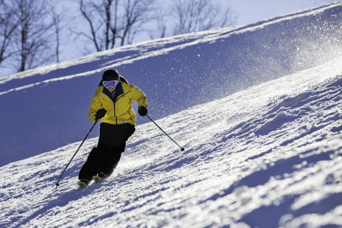 A skier in a yellow jacket skiing down a hill at Winterplace Ski Resort