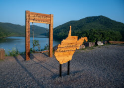 Rustic “Almost Heaven” swing and West Virginia sign overlooking Bluestone Lake and forested mountains.