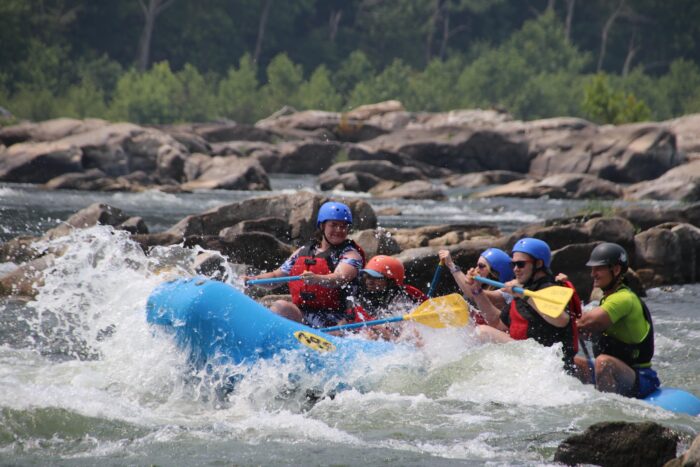 Close-up of a rafting group navigating a rocky rapid, with water splashing as they paddle a blue raft through a rugged whitewater section.