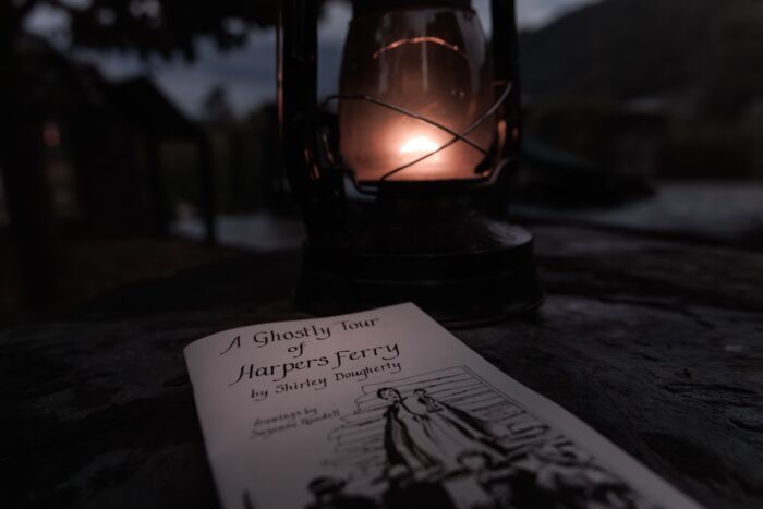 A copy of "A Ghostly Tour of Harpers Ferry" by Shirley Dougherty sits by an old-fashioned oil lantern