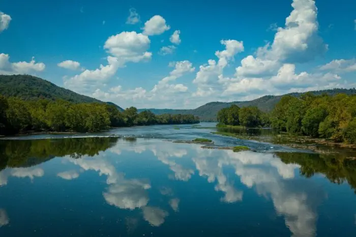 Calm river reflecting clouds and tree lined hills.