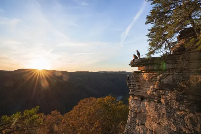 Hikers standing on cliff edge at sunset overlooking mountain valley.