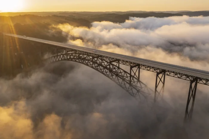 Bridge spanning fog filled gorge at sunrise.