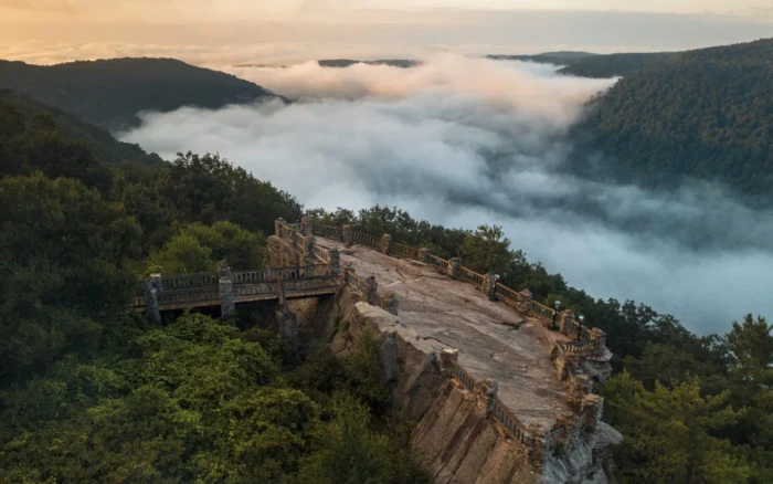 Stone overlook platform above valley filled with low clouds and forested hills