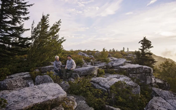 Two adults seated on rocky overlook surrounded by shrubs and trees